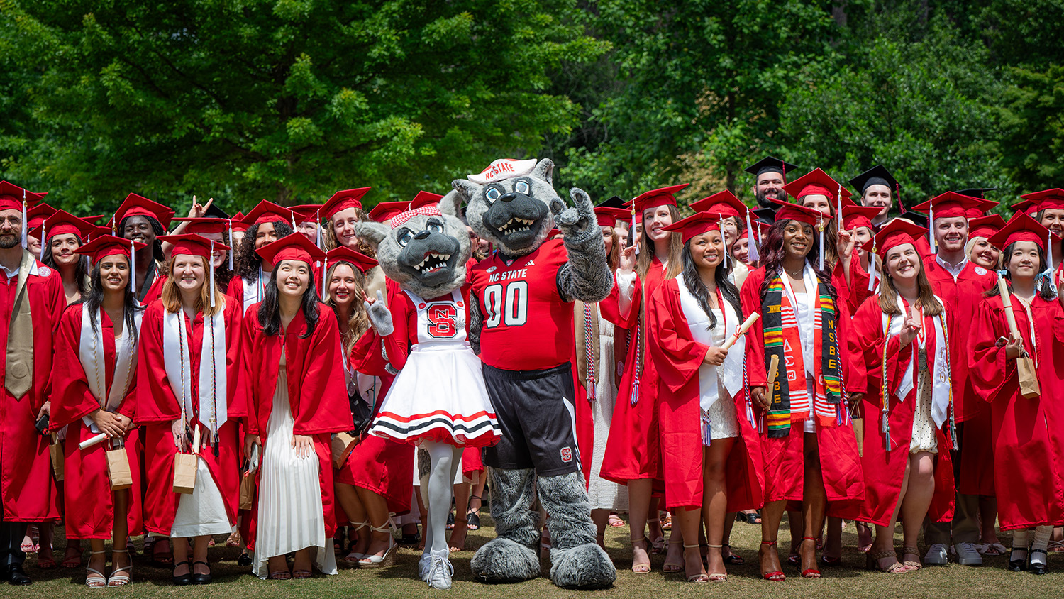 A crowd of graduates stand with Mr. Wuf and Ms. Wuf.