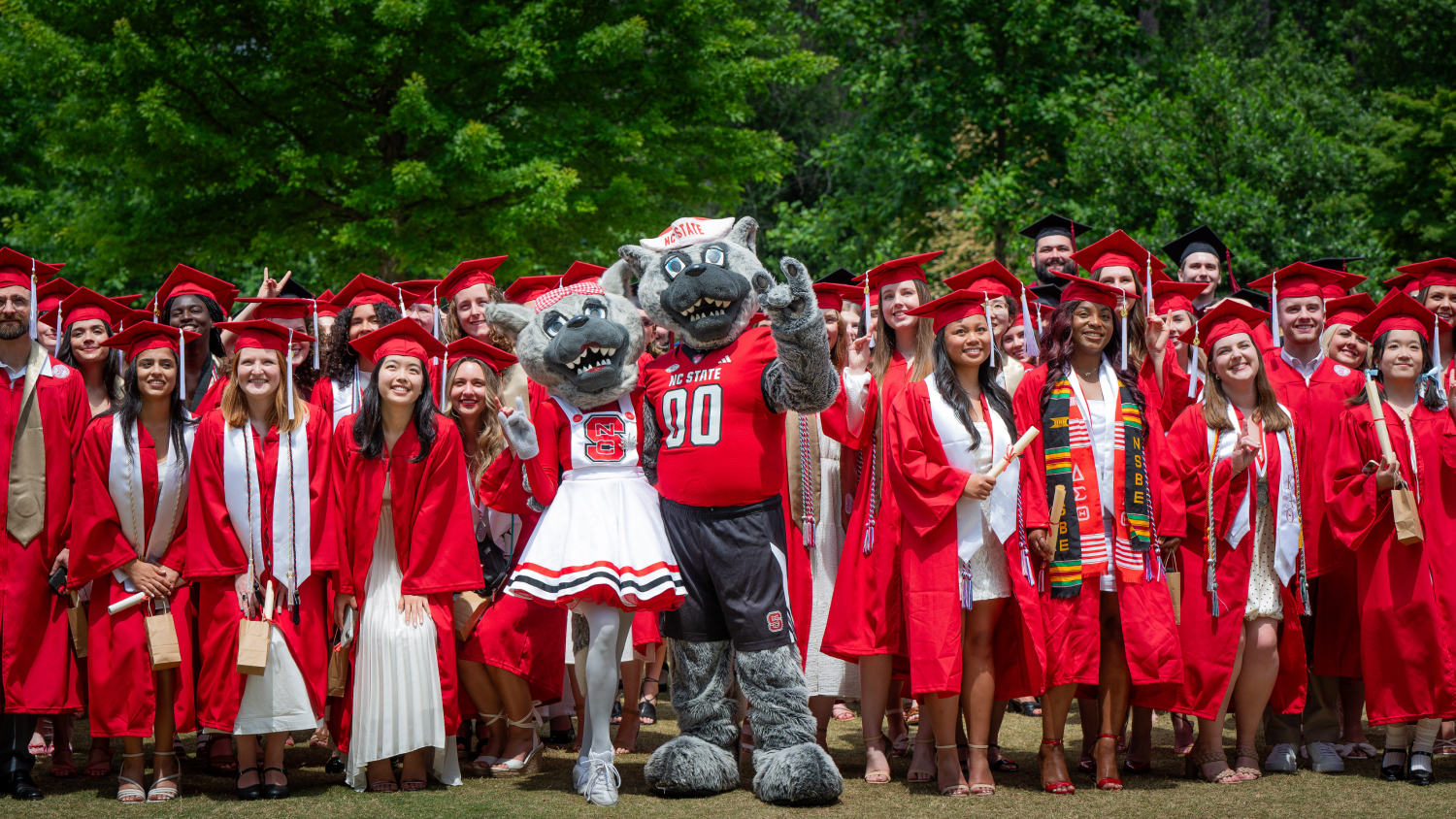 A crowd of graduates in red robes pose with Mr. and Ms. Wuf.